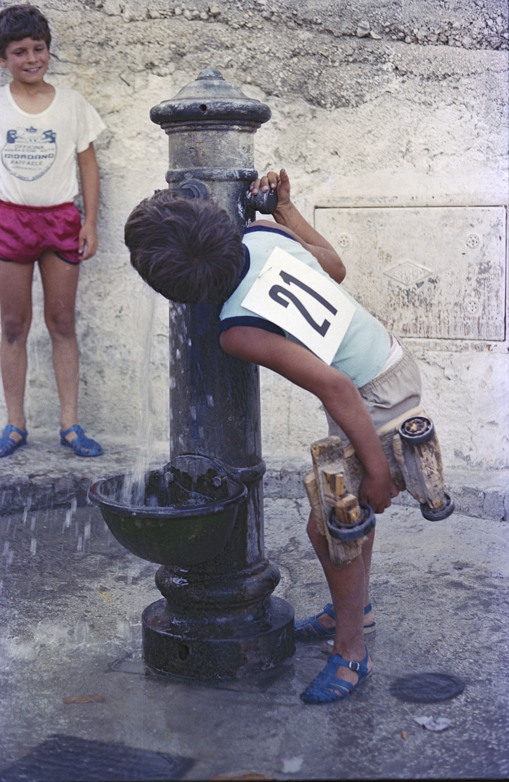 A boy drinking from a fountain in Monte Sant'Angelo with his sled